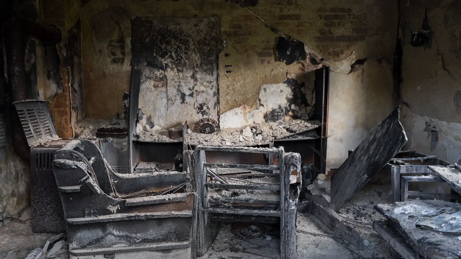 Interior de um imóvel comercial destruído por incêndio, com móveis carbonizados e cinzas, cenário típico do sinistro que o seguro empresarial deveria cobrir